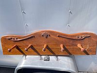 Front view of entire wooden coat rack showing five pegs and decorative top edge