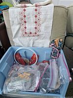 Overview of blue bin with yarn, hoop, needles and cross-stitch fabric draped