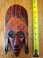 Front of carved hardwood mask beside tape measure