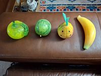 four fruit figurines lined up: glass apple, stone lime, stone pineapple, stone banana