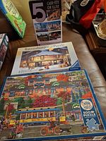 Three puzzle boxes displayed: Cobble Hill trolley scene, Ravensburger winter shop, 5-puzzle deluxe pack
