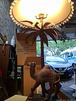 Full view of lit palm table lamp showing camel base, palm fronds and shade