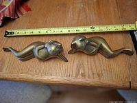 Both brass reclining frog figurines beside tape measure