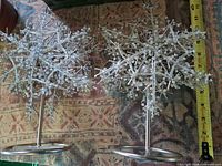 Pair of silver metal snowflake candleholders on ring bases beside measuring tape