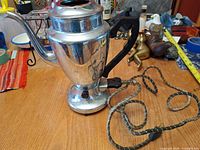 Side view of percolator showing chrome body, black handle, gooseneck spout and frayed cord