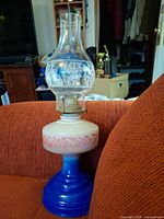 Full view of lamp showing blue base, milk glass font, brass burner, clear etched chimney