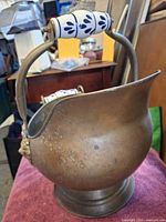 Side view of brass coal scuttle showing ceramic-grip bail handle and patina