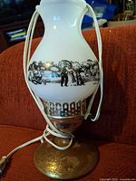 Front view of lamp showing milk glass shade with scene and metal base