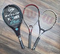 Front view of three tennis rackets on wood floor