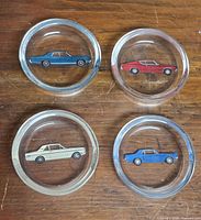 Front view of all four clear glass coasters displaying car graphics