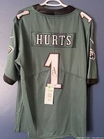 Full back view of jersey showing name HURTS, number 1, autograph, sleeve logos and COA tag