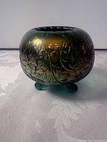 Front view of green iridescent glass bowl showing embossed floral pattern and three feet