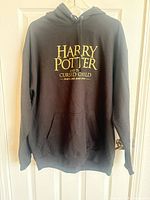 Front view of black hoodie showing yellow Harry Potter and the Cursed Child text and kangaroo pocket