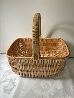 Side view of rectangular natural wicker basket showing fixed handle and weave pattern