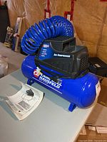 Full view of Campbell Hausfeld compressor with coiled hose and manual