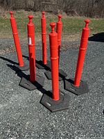 Six red plastic barrier posts standing on gravel surface, each in black hexagonal base