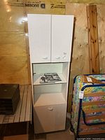 Full view of tall white melamine cabinet showing upper doors, open shelf, lower hamper door