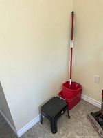 Step stool, one red bucket, mop handle leaning against wall