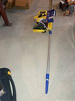 All four items on floor: extendable pole, tape reel, drill, glue gun