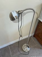 Full view of brushed metal gooseneck floor lamp standing on carpet