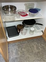 Cupboard view showing frying pan, Visions pot, roasting pan, stainless bowl, plastic containers and measuring cups
