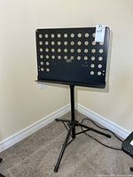 Full view of black perforated metal music stand on tripod base
