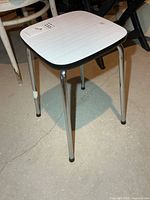 Overall view of stool showing chrome legs, white laminate seat and black edge trim