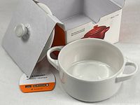 Open box showing white stoneware mini cocotte and lid still attached to cardboard insert.