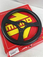 Front view of black suede MOMO Mod.69 steering wheel on red MOMO box