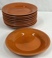 Stack of ten pumpkin-colored stoneware pasta bowls with one displayed