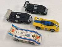 Top view of four Aurora AFX Magnatraction slot cars showing body styles and missing wheels on black cars