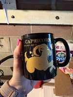 Front of black ceramic mug displaying gold Capricorn goat graphic and date range