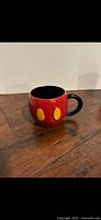 Side view of red Mickey Mouse themed ceramic mug showing yellow button accents, black handle and interior