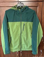 Front view of two-tone green hooded softshell jacket showing overall design, full zip, chest pocket and hand pockets