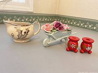 All four items: two red Swedish candlesticks, blue wheelbarrow figurine with roses, Lancaster & Sandland creamer