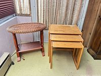 Three wooden nesting tables stacked together beside oval wicker and wood side table with magazine rack base