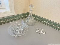 Three crystal items grouped: decanter with stopper, floral bowl, footed cake plate
