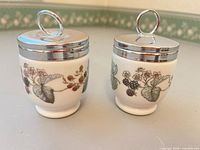 Front view of both egg coddlers showing blackberry design and chrome lids