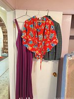 Three garments hanging on door: red wrap top, green tartan blazer, purple nightgown