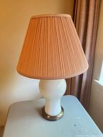 Full view of white ceramic lamp with pleated shade on brass base