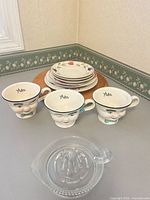 Wooden Cornwall tray, stacked plates, three Bailey's mugs, glass lemon squeezer