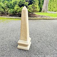 Full view of beige obelisk standing on pavement