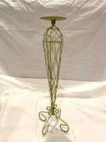 Full view of green metal candle stand with scroll base and ribbed candle plate