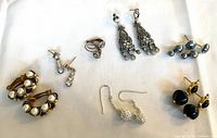 All seven pairs of earrings laid out on white cloth showing styles and materials