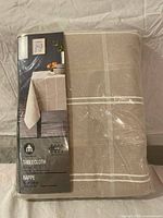 Front view of packaged beige tablecloth with plaid stripes and branding insert