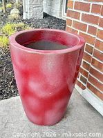 Full view of red tapered planter sitting outdoors on concrete