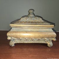 Side view of ornate gold-tone footed box with lid