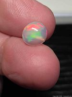 Opal cabochon showing play-of-color on fingertip