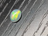 Opal cabochon resting on textured surface showing play-of-colour