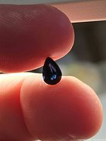 Pear-cut deep blue spinel held between fingers, showing overall size and color